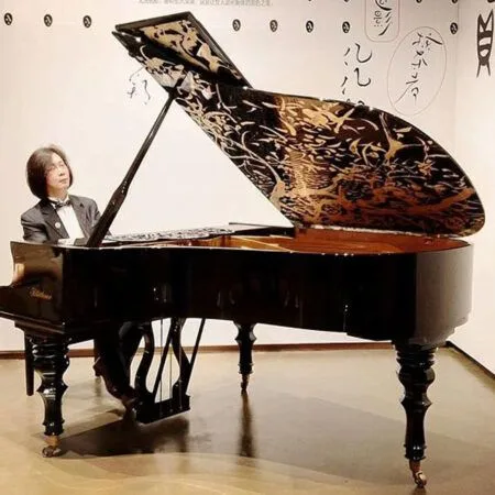 Musician playing an ornately decorated grand piano on stage.
