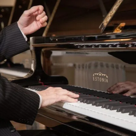 Hands playing a grand piano with focus on the keys and strings.