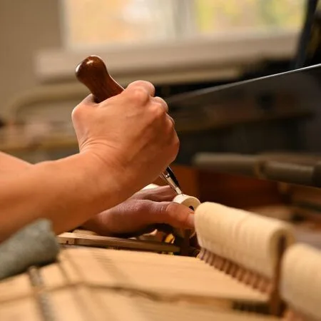 Hands tuning a piano with a tuning hammer.