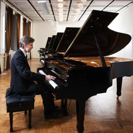 Man playing a grand piano in a spacious room.