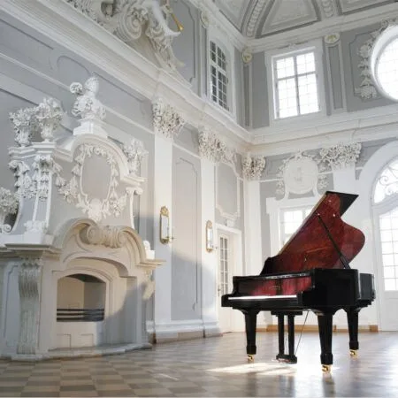 Elegant grand piano in a bright, ornate white room with classical decor.
