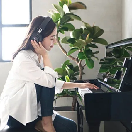 Young woman playing piano with headphones on in a bright room.