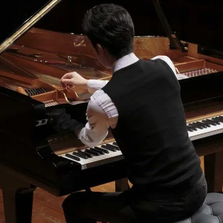 A man playing a grand piano, viewed from behind.