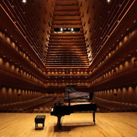 Grand piano on stage in a large, architecturally intricate concert hall.