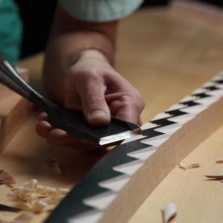 Close-up of hand carving patterned wood with a chisel.