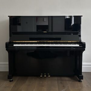 A sleek black upright piano against a white wall with wooden flooring.
