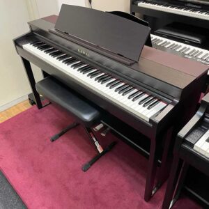 A sleek black digital piano with matching bench on a red carpet.