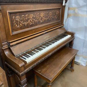 Antique upright piano with intricate wood carvings and a matching bench.