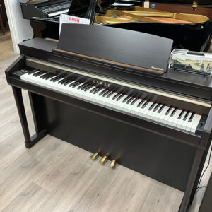 Digital piano with three pedals on a wooden floor.