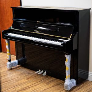 A black upright piano with protective covers on its legs.
